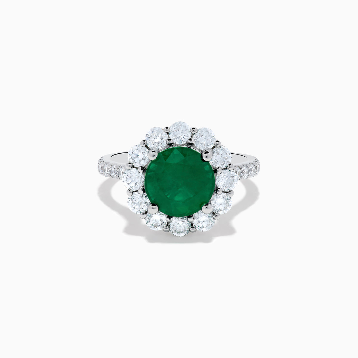 The 18K White Gold Emerald and Diamond Halo Ring features a large round green emerald center, surrounded by sparkling diamonds on the halo and band, beautifully displayed on a white background.