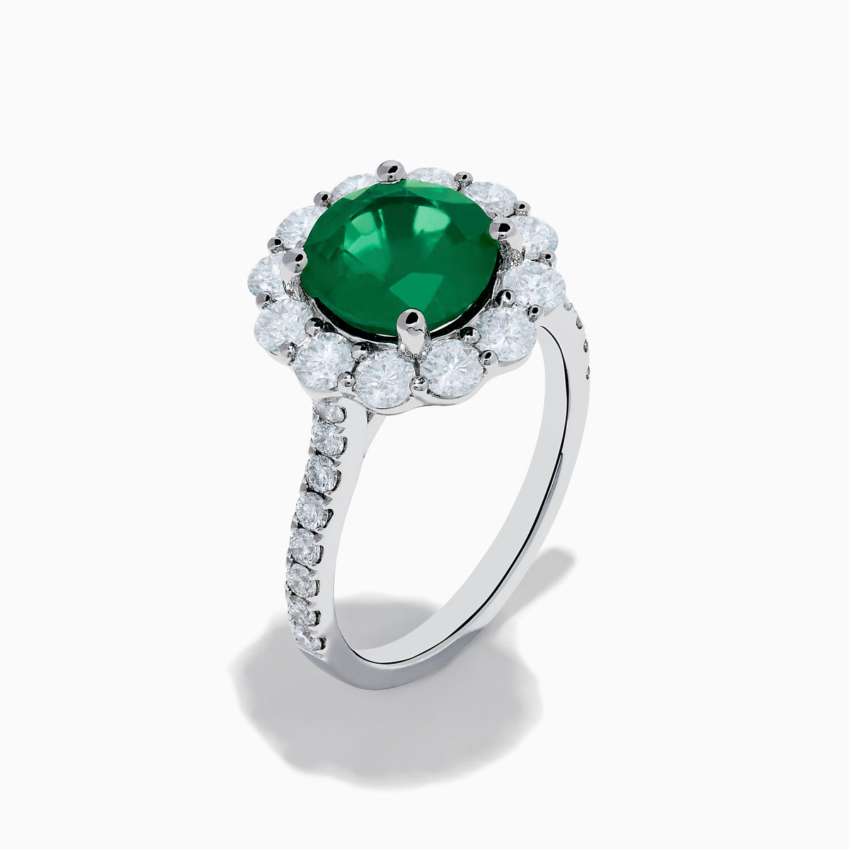 The 18K White Gold Emerald and Diamond Halo Ring features a large round green emerald center, surrounded by sparkling diamonds on the halo and band, beautifully displayed on a white background.