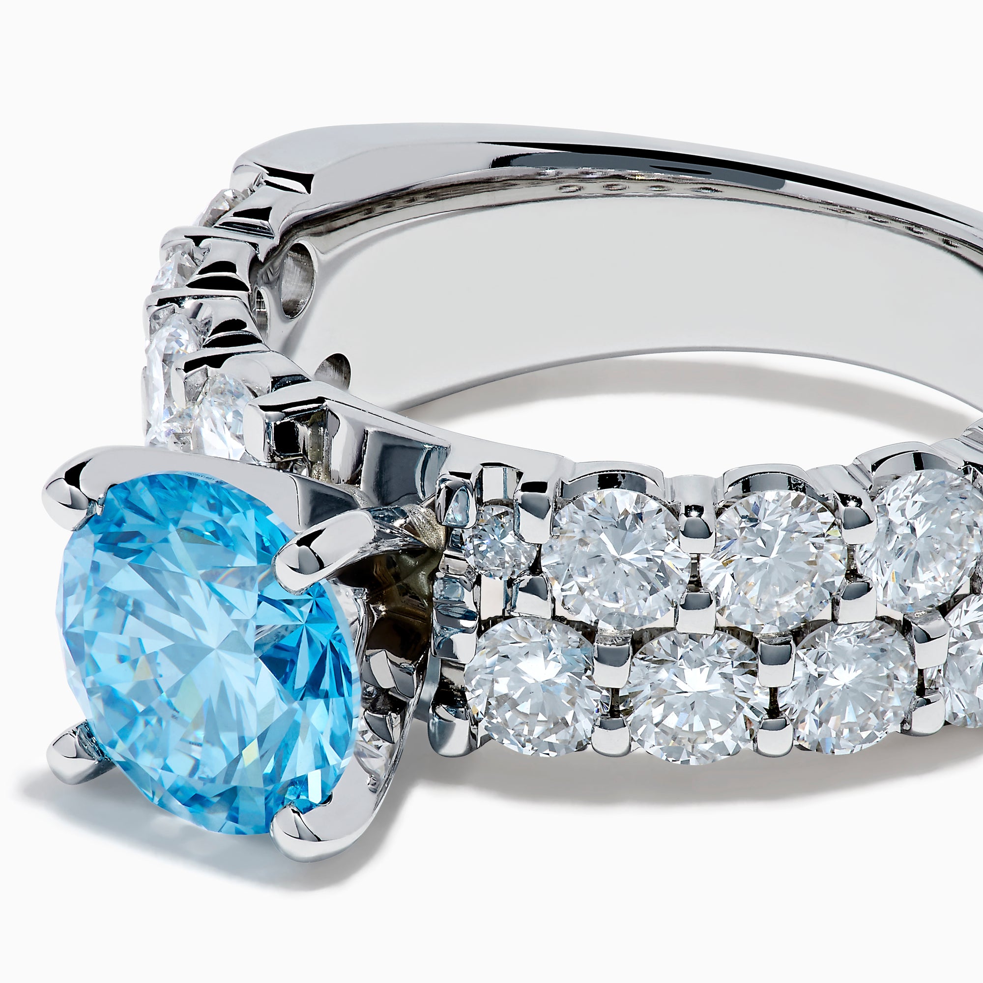 The Lab Grown Blue Diamond Round Brilliant Solitaire Ring in 14K White Gold features a striking round blue diamond center, accented by two rows of sparkling clear diamonds along the band, shown on a white background.