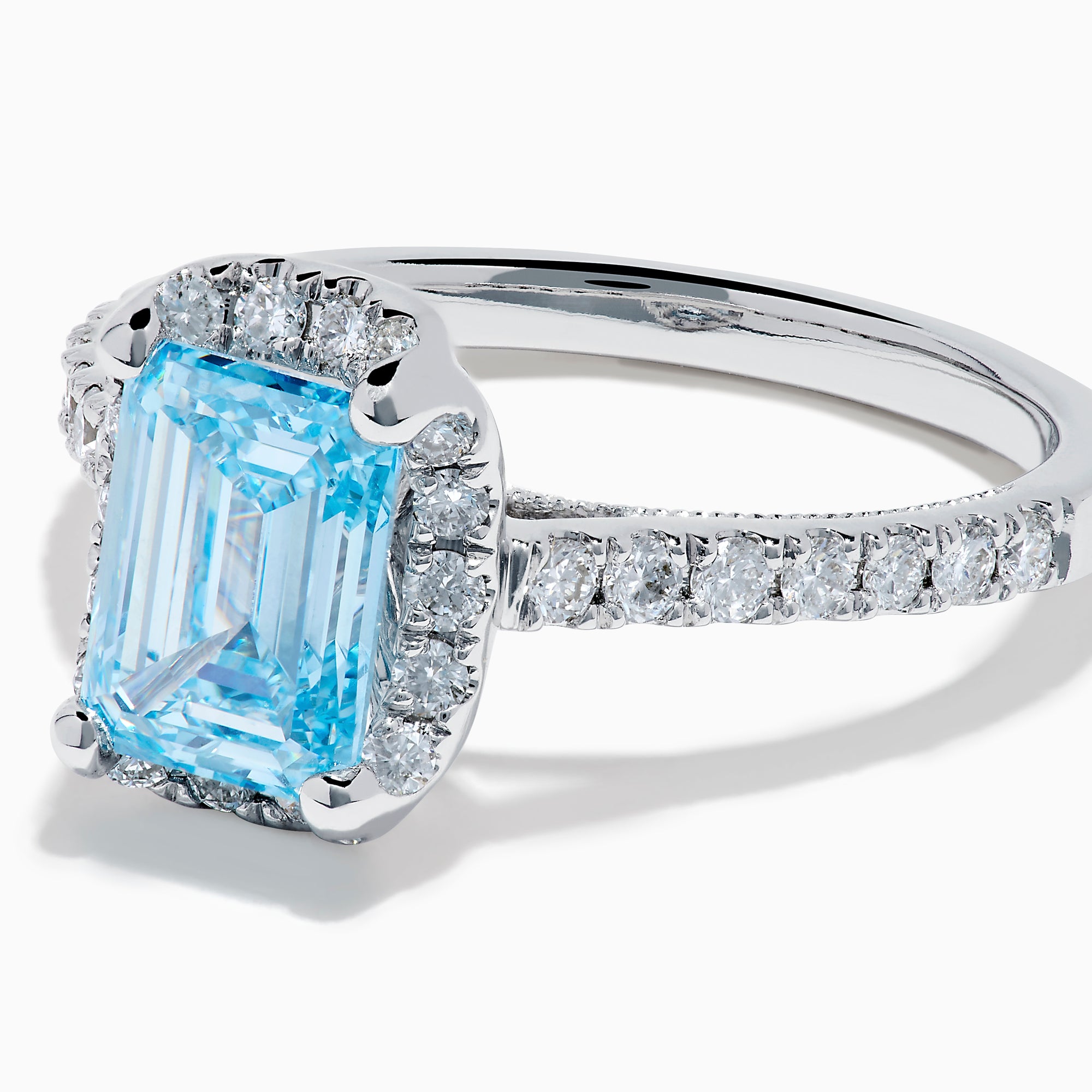 The Lab Grown Blue and White Diamond Halo Ring in 14K White Gold features an emerald-cut blue center stone with lab grown diamond accents, beautifully showcased on a white background.