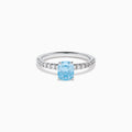 The Lab Grown Blue Diamond Solitaire Cushion Ring in 14K White Gold features a rectangular lab grown blue diamond at the center, accented with small clear round stones along the band.