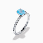 The Lab Grown Blue Diamond Solitaire Cushion Ring in 14K White Gold features a rectangular lab grown blue diamond at the center, accented with small clear round stones along the band.