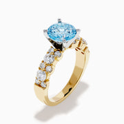 The Lab Grown Blue and White Diamond Ring in 14K Yellow Gold showcases a large round light blue gemstone at the center, accented by three teardrop-shaped lab grown white diamonds on each side.