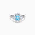 The Lab Grown Blue and White Diamond Ring in 14K White Gold showcases an oval blue gemstone surrounded by a halo of lab grown diamonds, with more diamonds accenting the band.