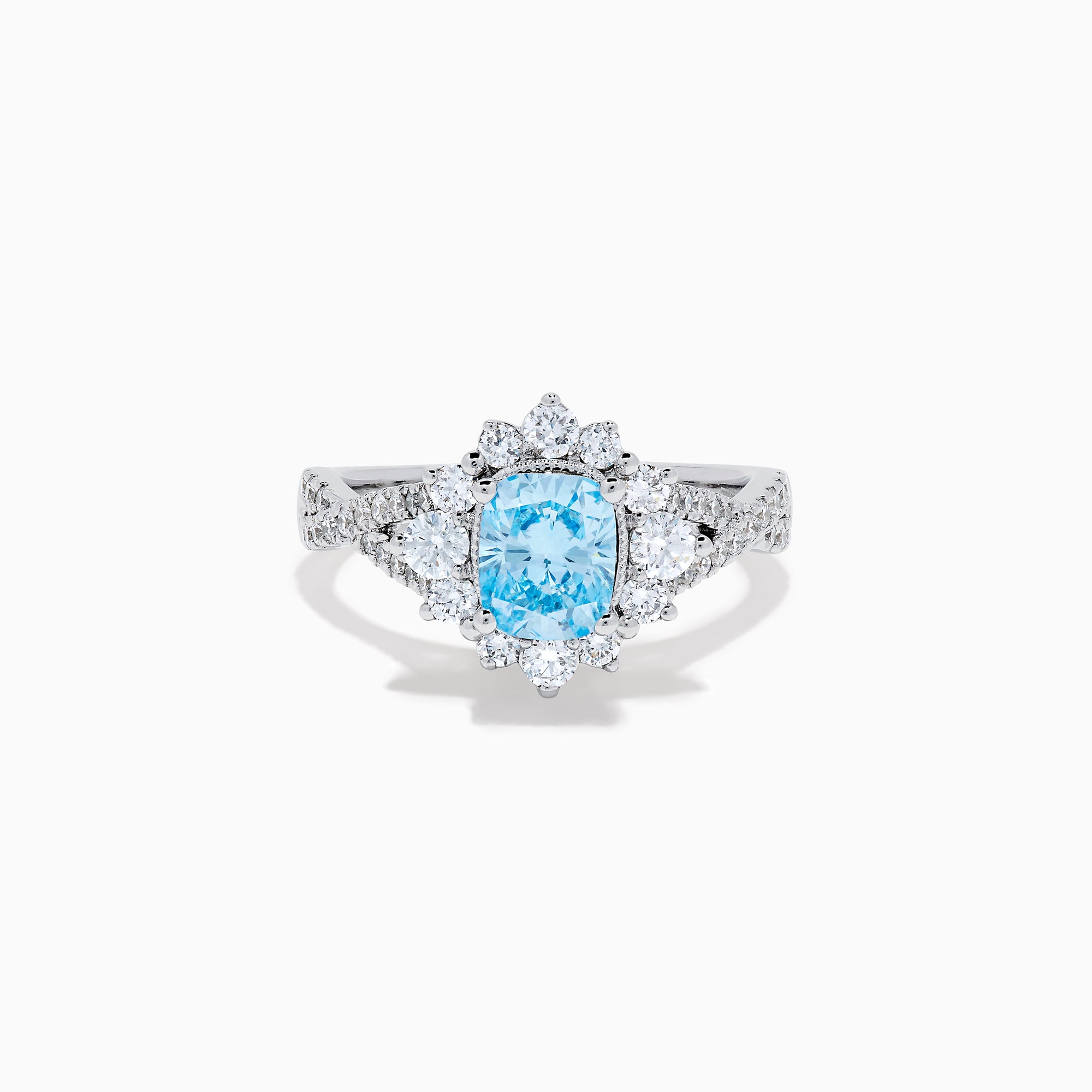 The Lab Grown Blue and White Diamond Ring in 14K White Gold showcases an oval blue gemstone surrounded by a halo of lab grown diamonds, with more diamonds accenting the band.