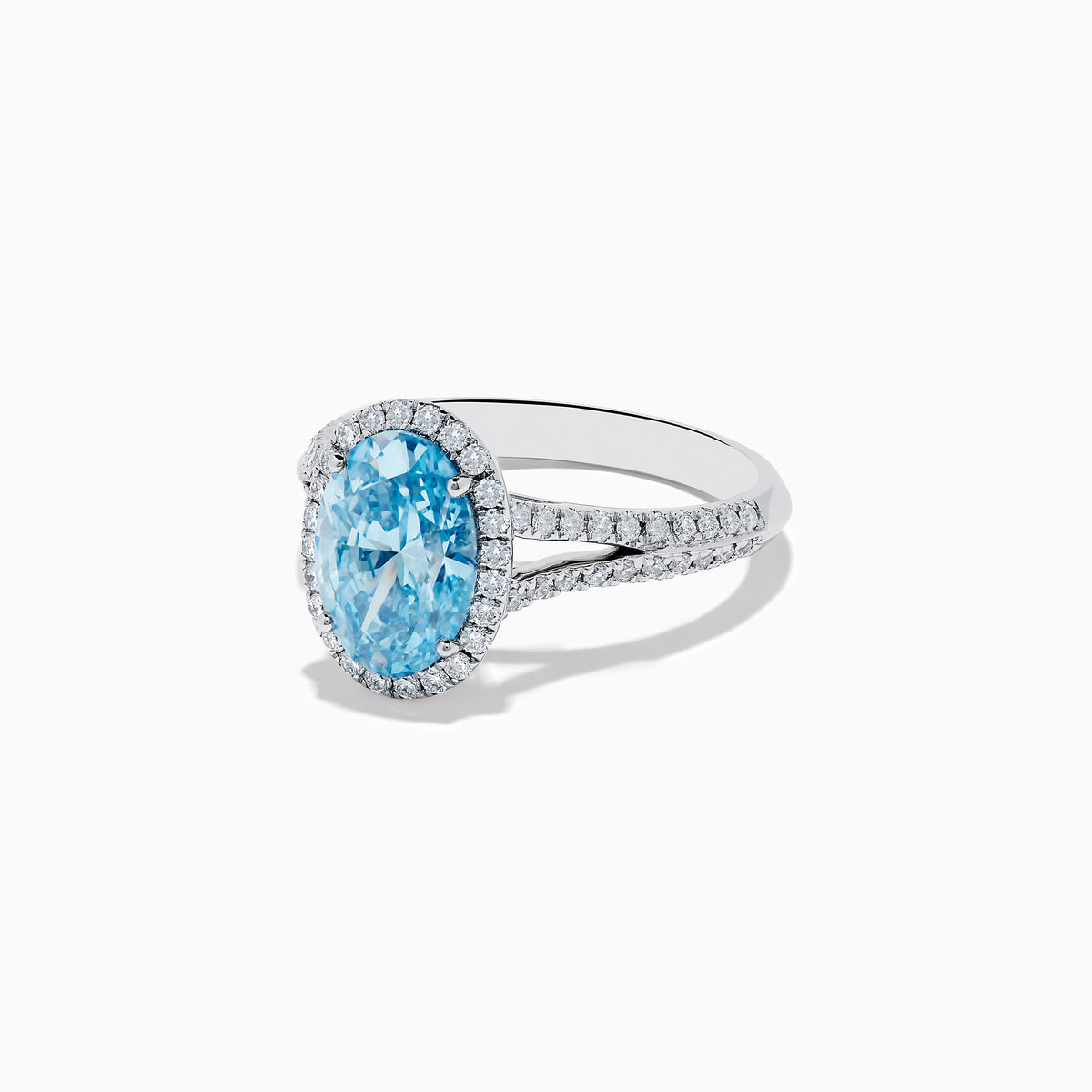 The 14K White Gold Lab Grown Blue and White Diamond Ring showcases an oval blue center stone, a halo of blue and white diamonds, and extra diamonds along the band for stunning brilliance.