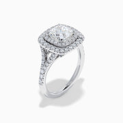 The Lab Grown Cushion Diamond Double Halo Ring in 14K White Gold features a cushion-cut center diamond, double halo of smaller diamonds, and additional diamonds along the band.