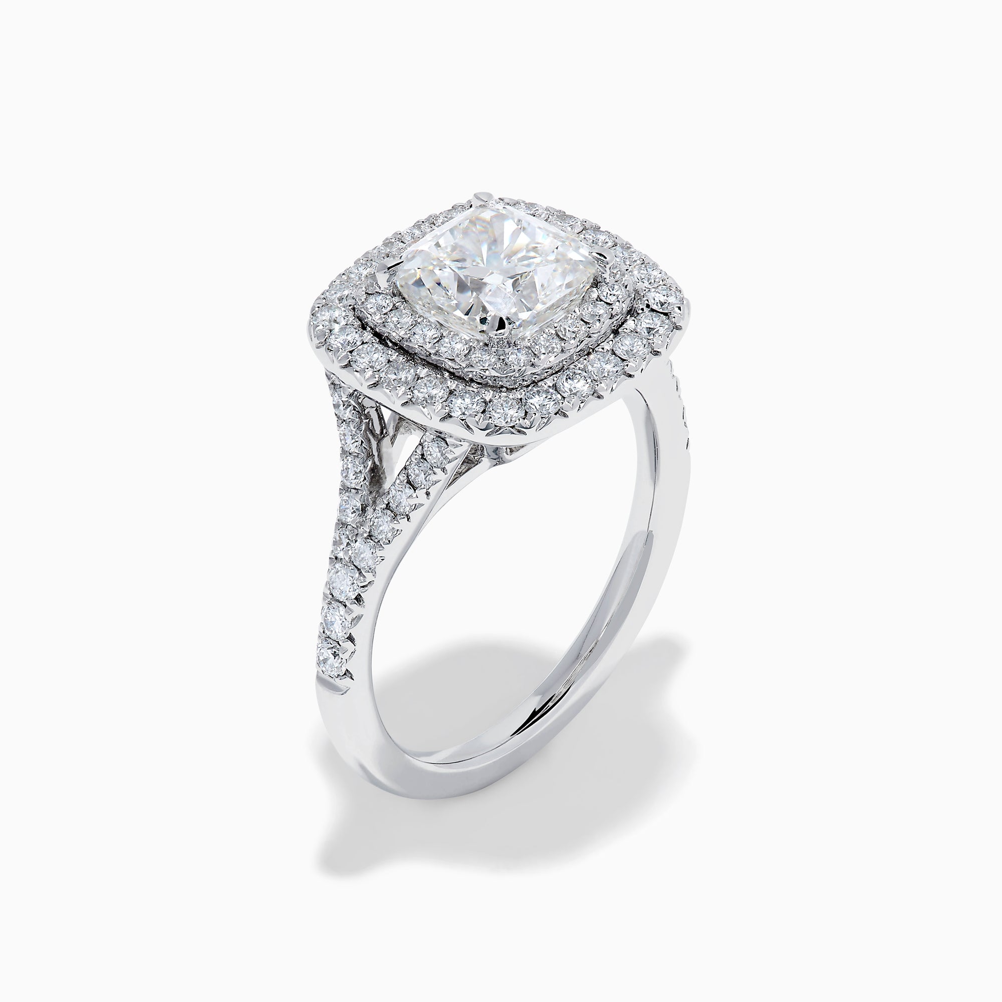 The Lab Grown Cushion Diamond Double Halo Ring in 14K White Gold features a cushion-cut center diamond, double halo of smaller diamonds, and additional diamonds along the band.