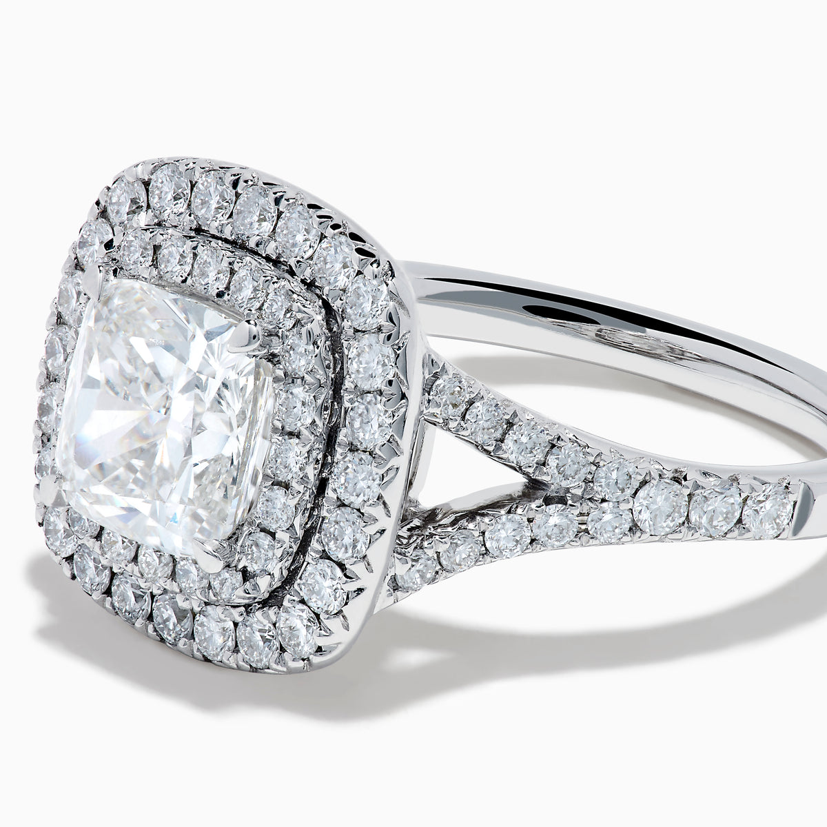 The Lab Grown Cushion Diamond Double Halo Ring in 14K White Gold features a cushion-cut center diamond, double halo of smaller diamonds, and additional diamonds along the band.