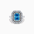 The Lab Grown Blue Diamond Double Halo Cocktail Ring in 14K White Gold features a rectangular blue center, round white diamonds on the band, and is displayed against a white background.