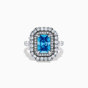The Lab Grown Blue Diamond Double Halo Cocktail Ring in 14K White Gold features a rectangular blue center, round white diamonds on the band, and is displayed against a white background.