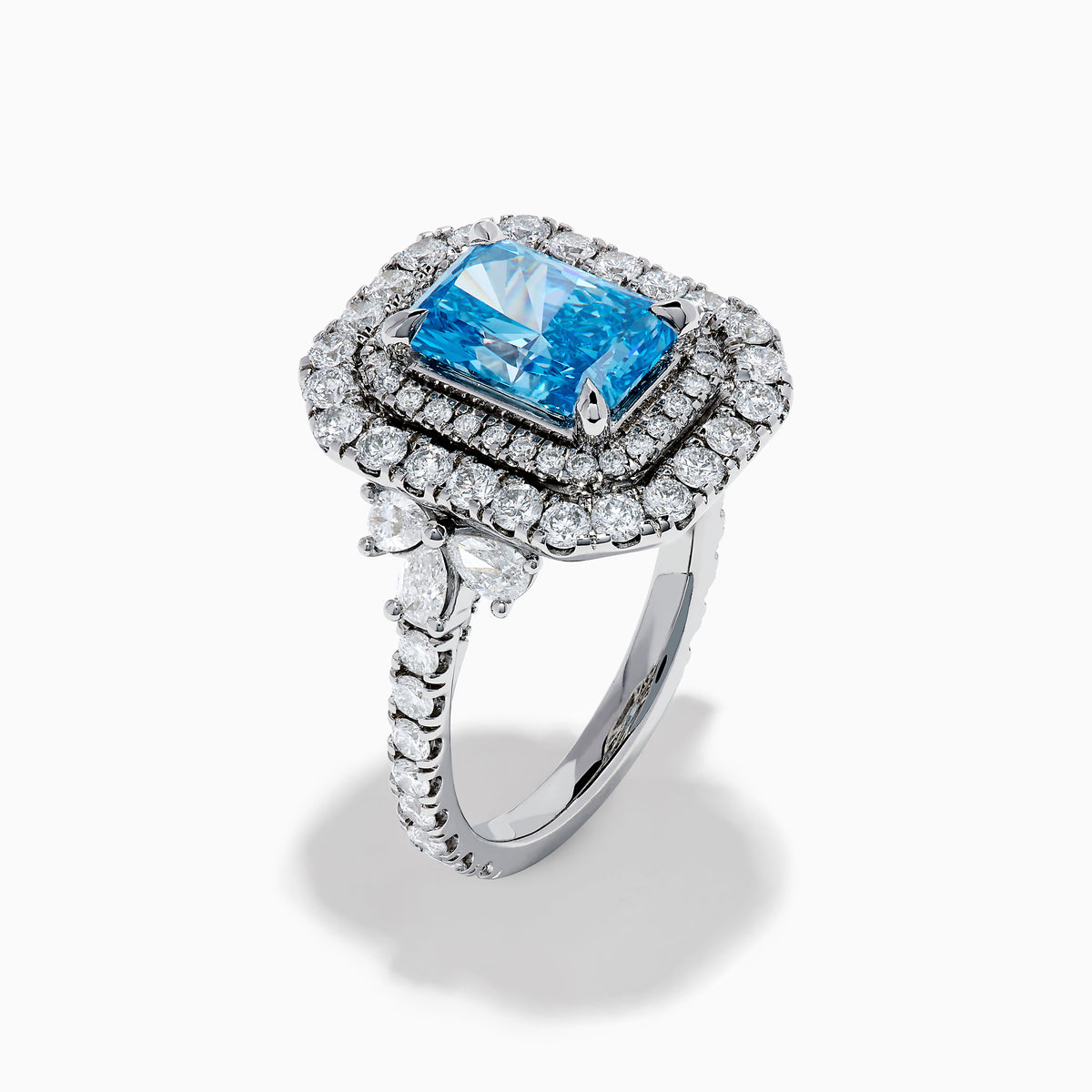 The Lab Grown Blue Diamond Double Halo Cocktail Ring in 14K White Gold features a rectangular blue center, round white diamonds on the band, and is displayed against a white background.