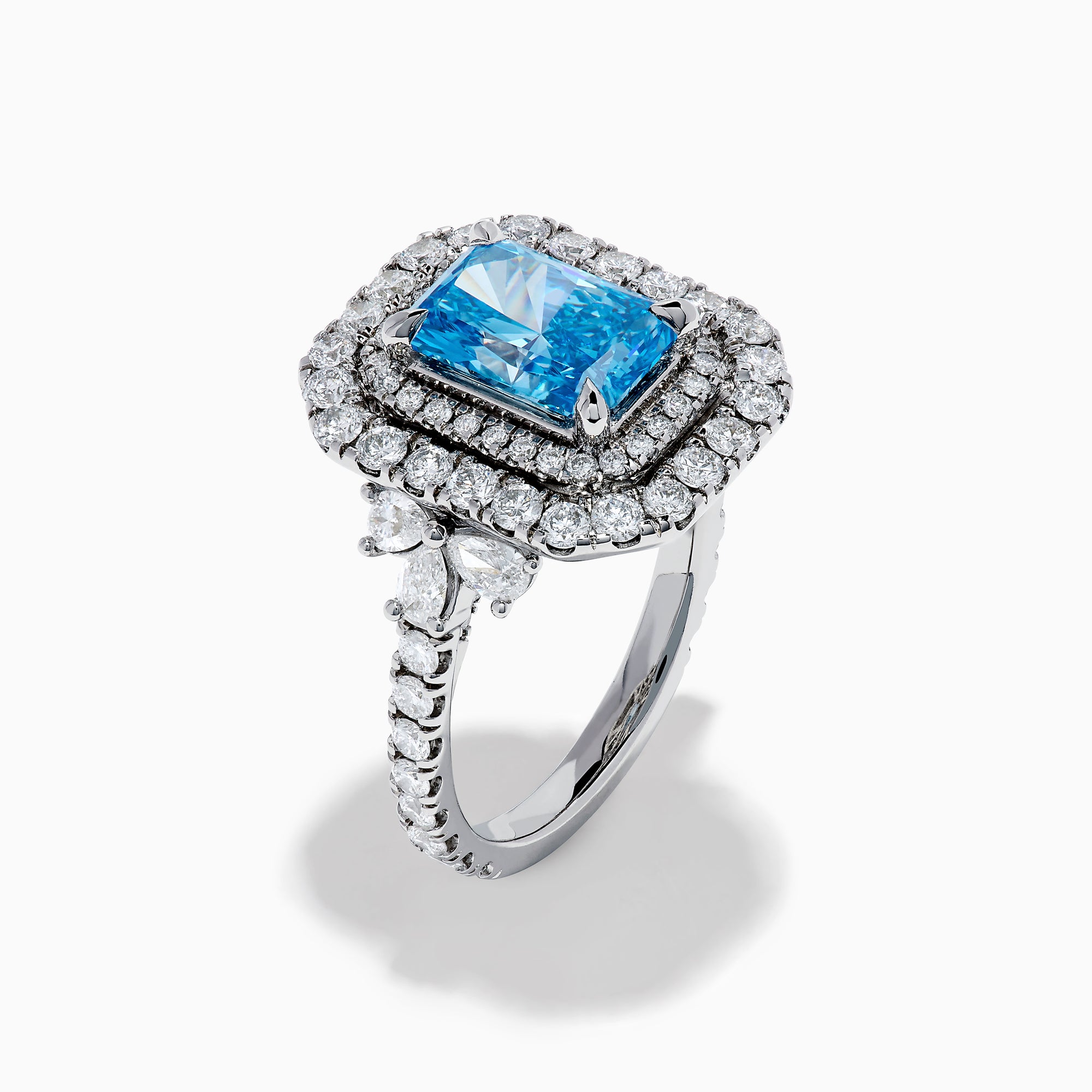 The Lab Grown Blue Diamond Double Halo Cocktail Ring in 14K White Gold features a rectangular blue center, round white diamonds on the band, and is displayed against a white background.