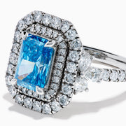 The Lab Grown Blue Diamond Double Halo Cocktail Ring in 14K White Gold features a rectangular blue center, round white diamonds on the band, and is displayed against a white background.
