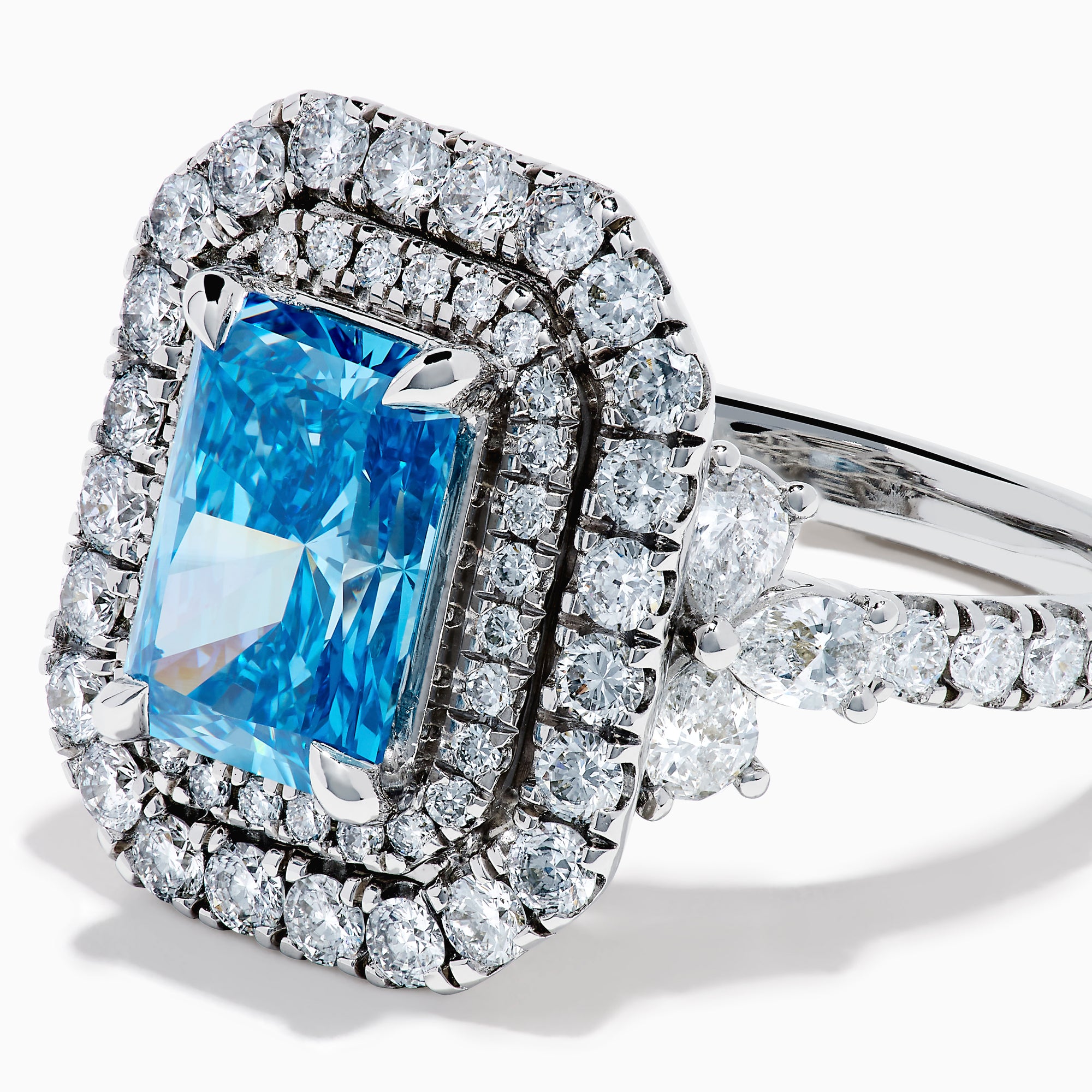 The Lab Grown Blue Diamond Double Halo Cocktail Ring in 14K White Gold features a rectangular blue center, round white diamonds on the band, and is displayed against a white background.