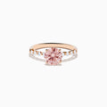 The 14K Rose Gold Lab Grown Pink and White Diamond Ring showcases a large round pink and white diamond centered between three smaller clear stones on each side, set against a plain white background.