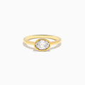 The Lab Grown Diamond East West Oval Ring in 14K Yellow Gold showcases a single lab diamond in a sleek bezel setting, presented against a plain white background.