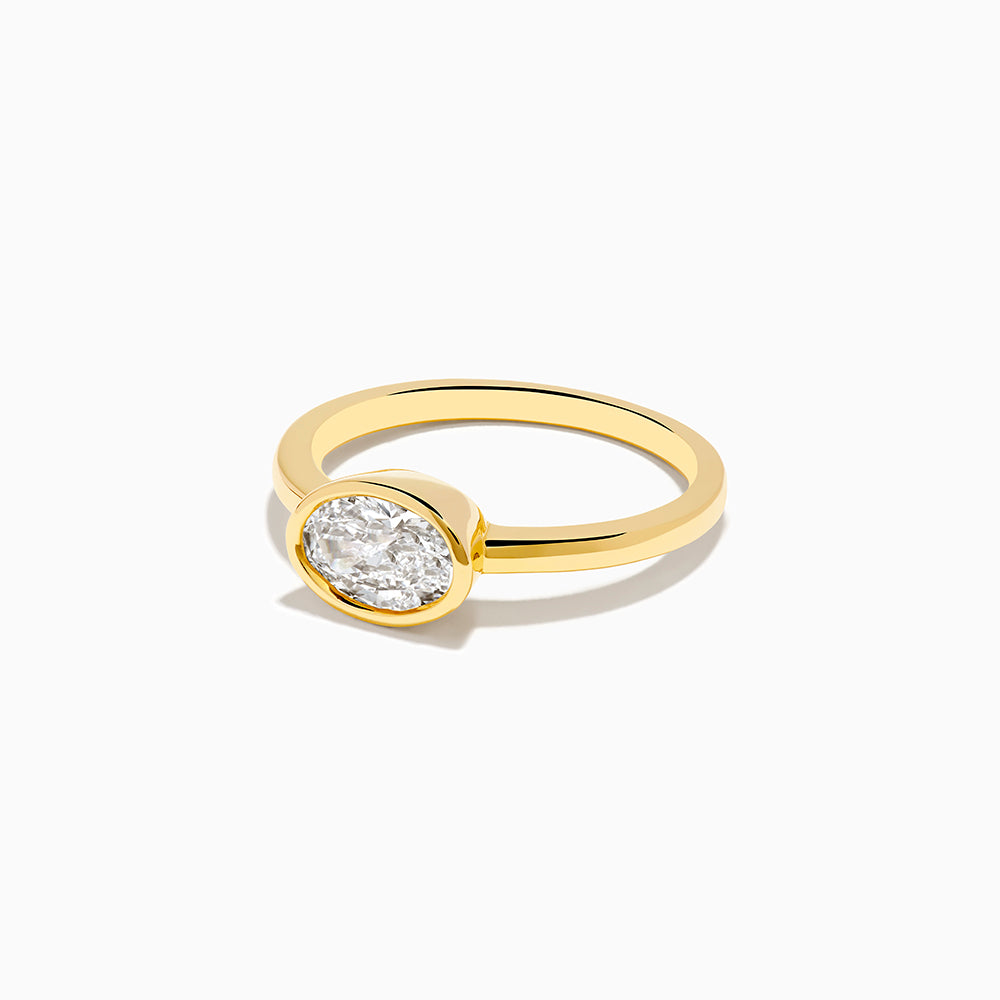 The Lab Grown Diamond East West Oval Ring in 14K Yellow Gold showcases a single lab diamond in a sleek bezel setting, presented against a plain white background.