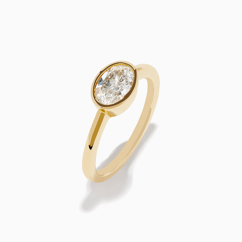 The Lab Grown Diamond East West Oval Ring in 14K Yellow Gold showcases a single lab diamond in a sleek bezel setting, presented against a plain white background.