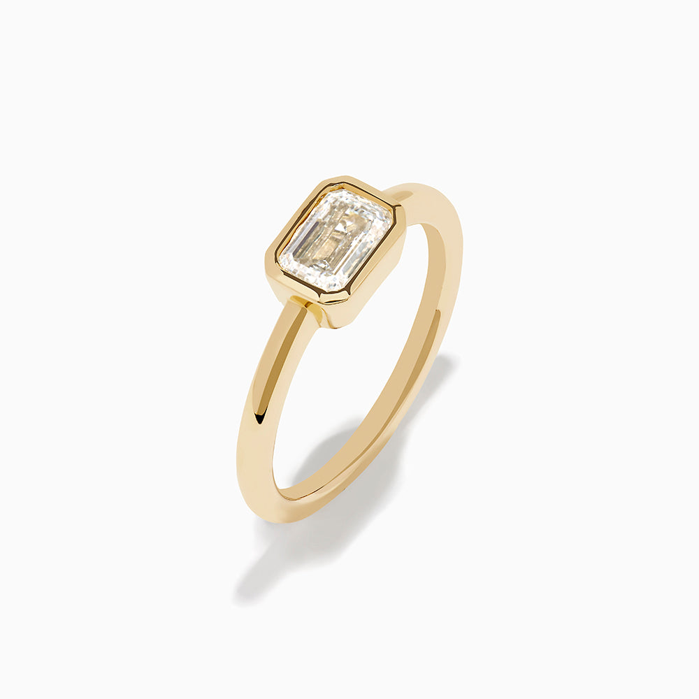 The Lab Grown Diamond East West Emerald-Cut Ring in 14K Yellow Gold features a lab diamond in a minimalist bezel setting, beautifully crafted and shown against a plain white background.