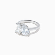 The Lab Grown Diamond Toi Et Moi Ring in 14K White Gold showcases emerald-cut and pear-shaped lab diamonds set side by side on a sleek band, displayed against a white background.