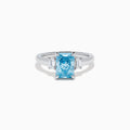 The Lab Grown Blue Diamond 3-Stone Ring in 14K White Gold features a brilliant blue center diamond with two clear rectangular side stones, set in sleek white gold against a crisp white background.