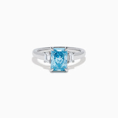 The Lab Grown Blue Diamond 3-Stone Ring in 14K White Gold features a brilliant blue center diamond with two clear rectangular side stones, set in sleek white gold against a crisp white background.