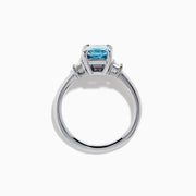 The Lab Grown Blue Diamond 3-Stone Ring in 14K White Gold features a brilliant blue center diamond with two clear rectangular side stones, set in sleek white gold against a crisp white background.