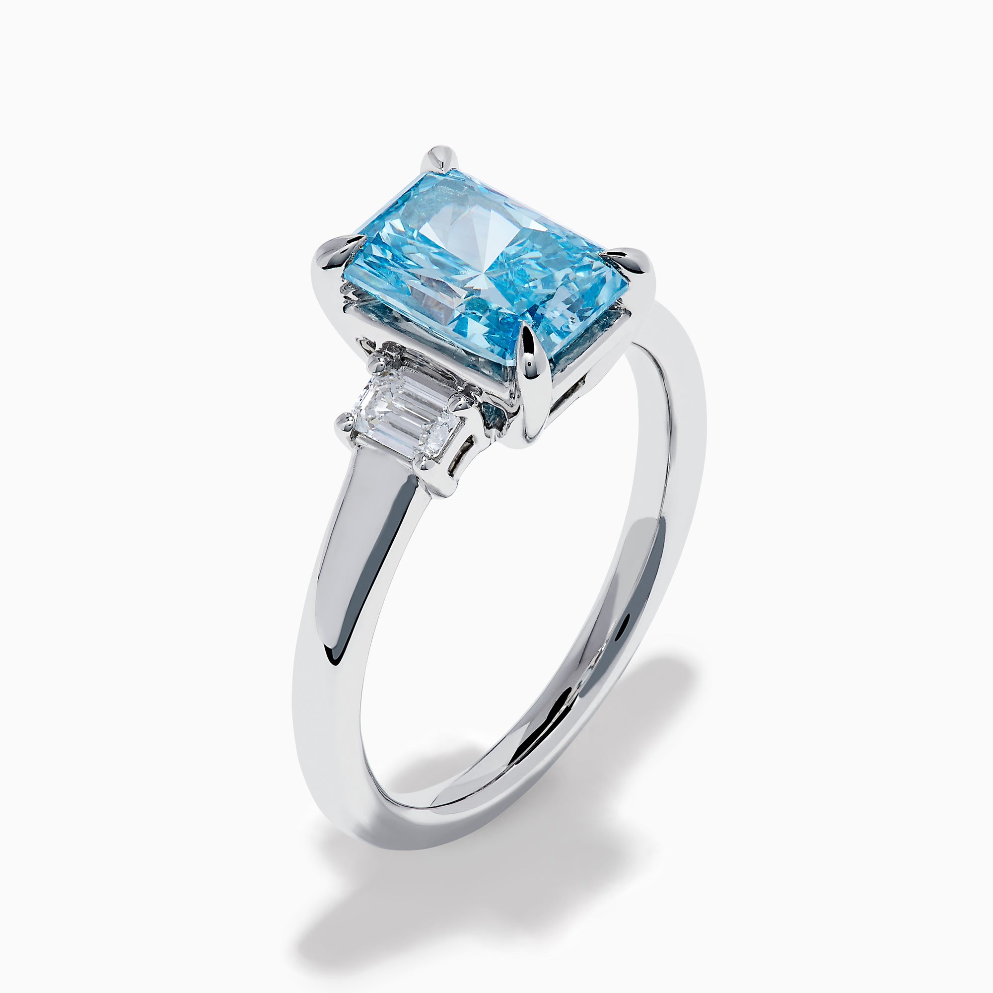 The Lab Grown Blue Diamond 3-Stone Ring in 14K White Gold features a brilliant blue center diamond with two clear rectangular side stones, set in sleek white gold against a crisp white background.