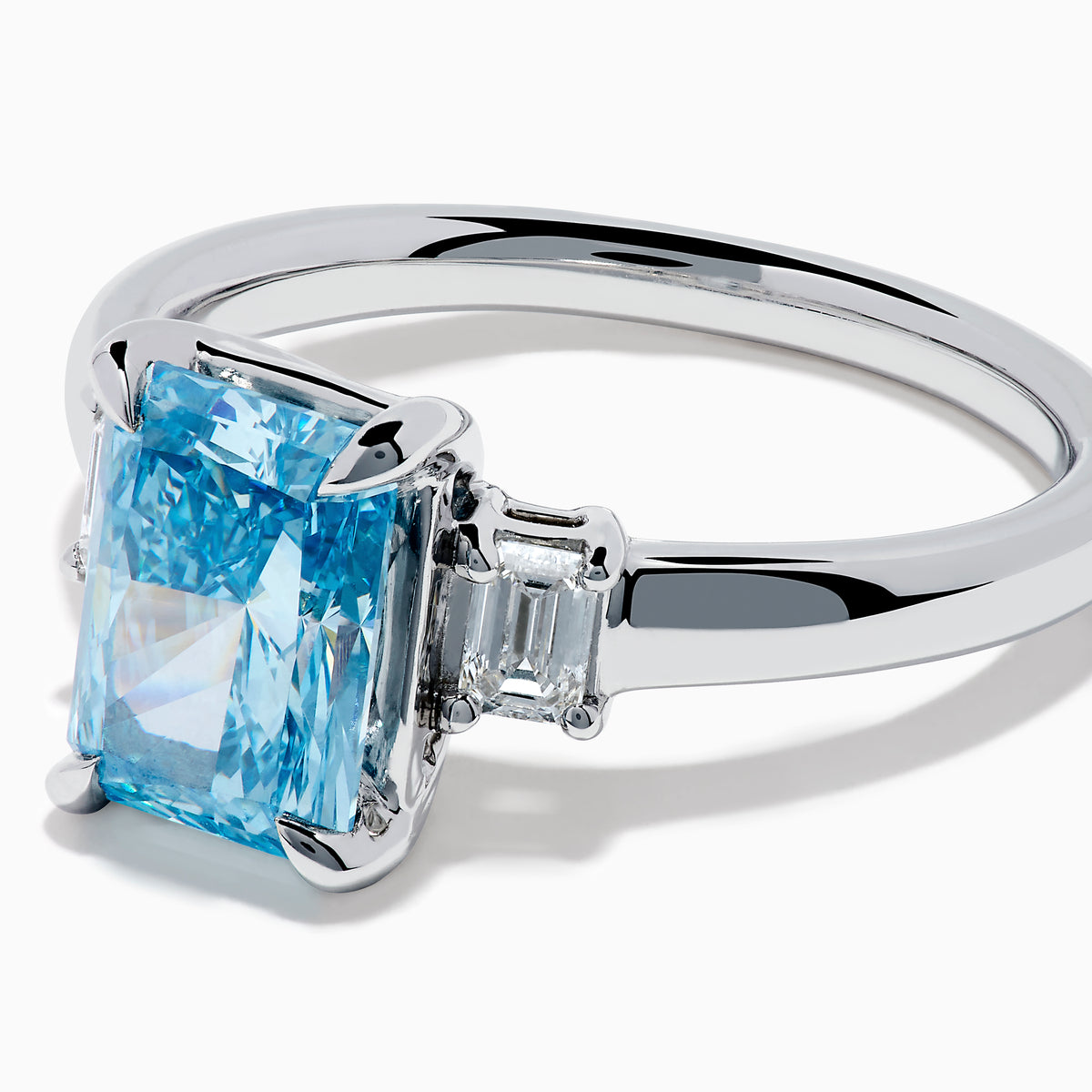 The Lab Grown Blue Diamond 3-Stone Ring in 14K White Gold showcases a large rectangular blue diamond center stone and a smaller clear rectangular side stone, all set in sleek white gold against a white background.