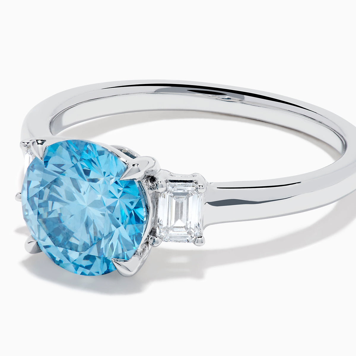 The Lab Grown Blue and White Diamond 3 Stone Ring in 14K White Gold features a striking round blue gemstone center with two rectangular lab grown diamonds on each side, all set in elegant white gold.