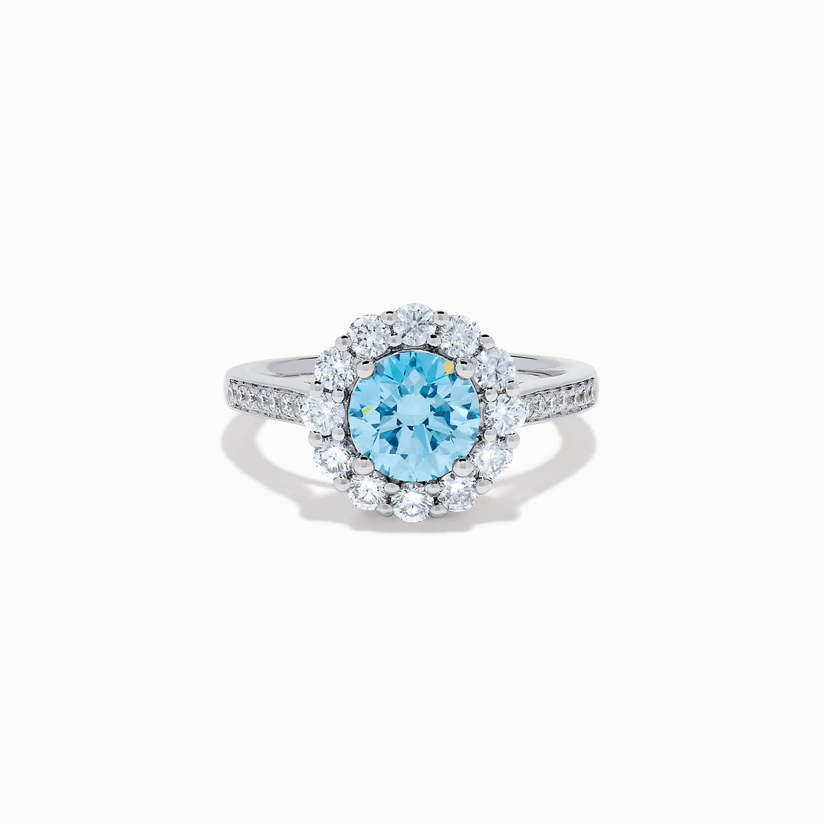 The Lab Grown Blue and White Diamond Halo Ring in 14K White Gold showcases a striking round blue center stone, encircled by lab grown diamond accents and additional diamonds adorning the band.