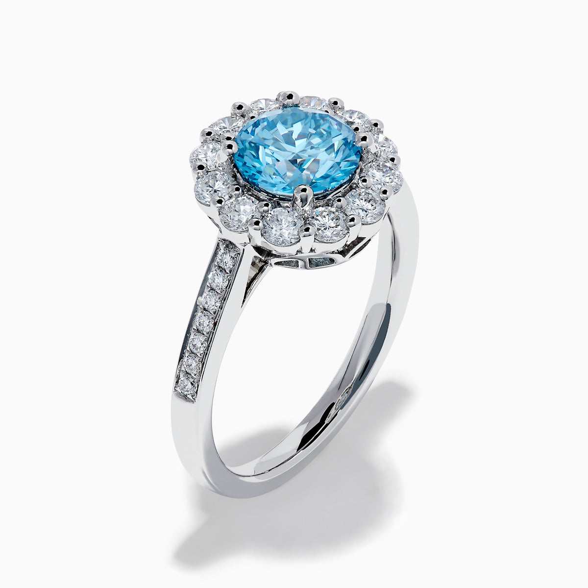 The Lab Grown Blue and White Diamond Halo Ring in 14K White Gold showcases a striking round blue center stone, encircled by lab grown diamond accents and additional diamonds adorning the band.