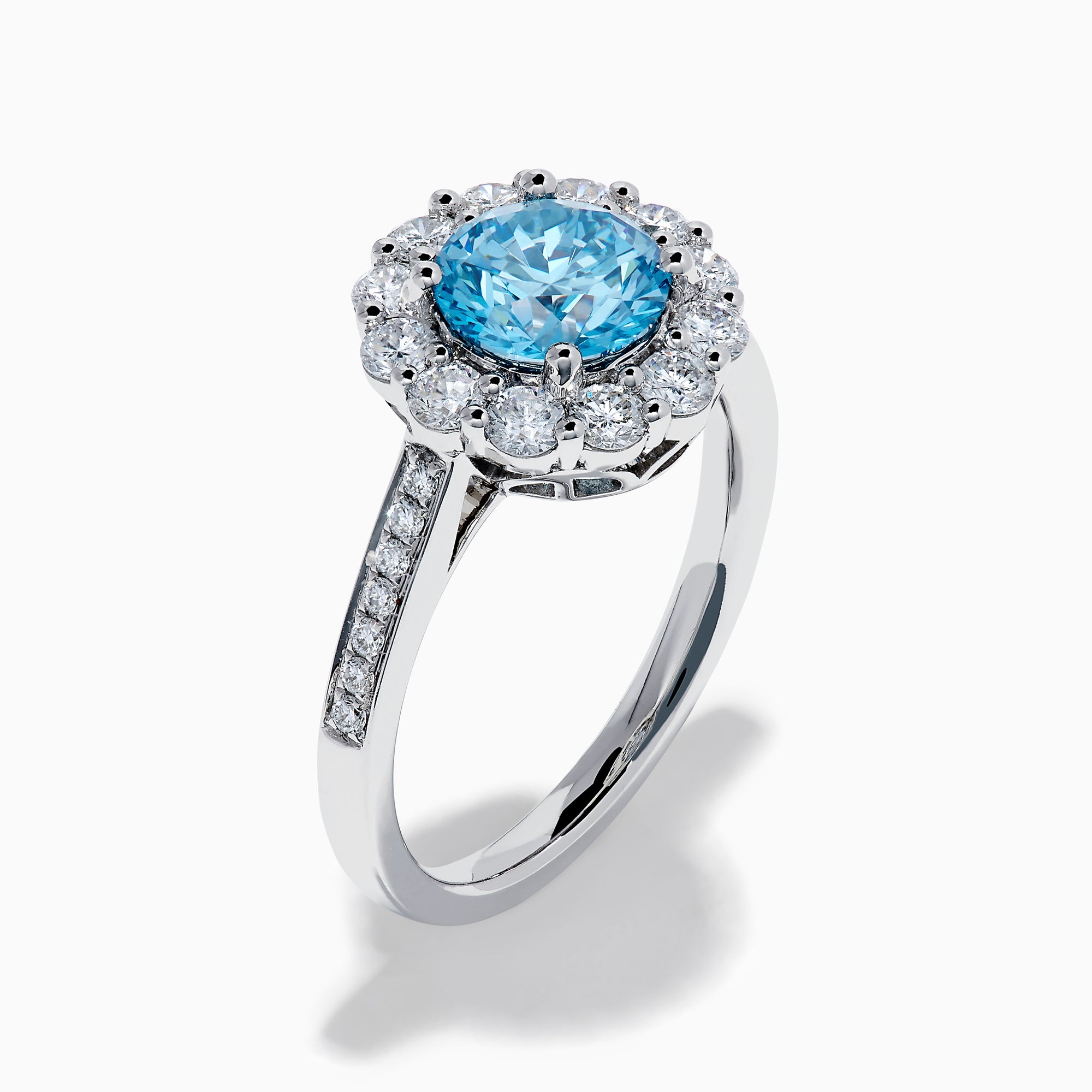 The Lab Grown Blue and White Diamond Halo Ring in 14K White Gold showcases a striking round blue center stone, encircled by lab grown diamond accents and additional diamonds adorning the band.