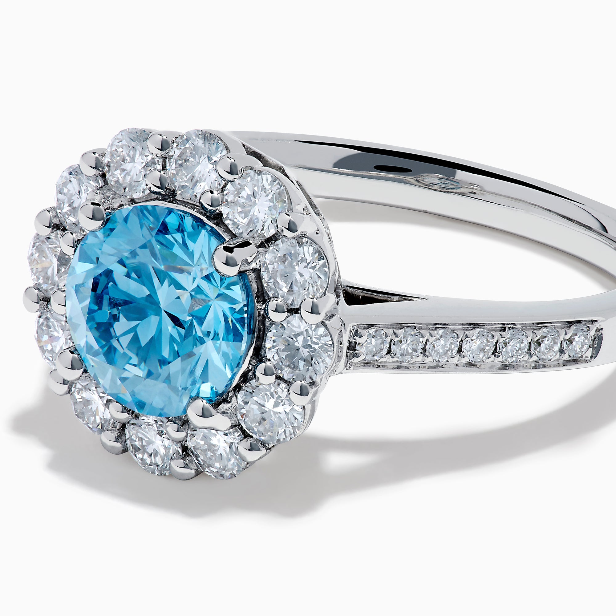 The Lab Grown Blue and White Diamond Halo Ring in 14K White Gold showcases a striking round blue center stone, encircled by lab grown diamond accents and additional diamonds adorning the band.