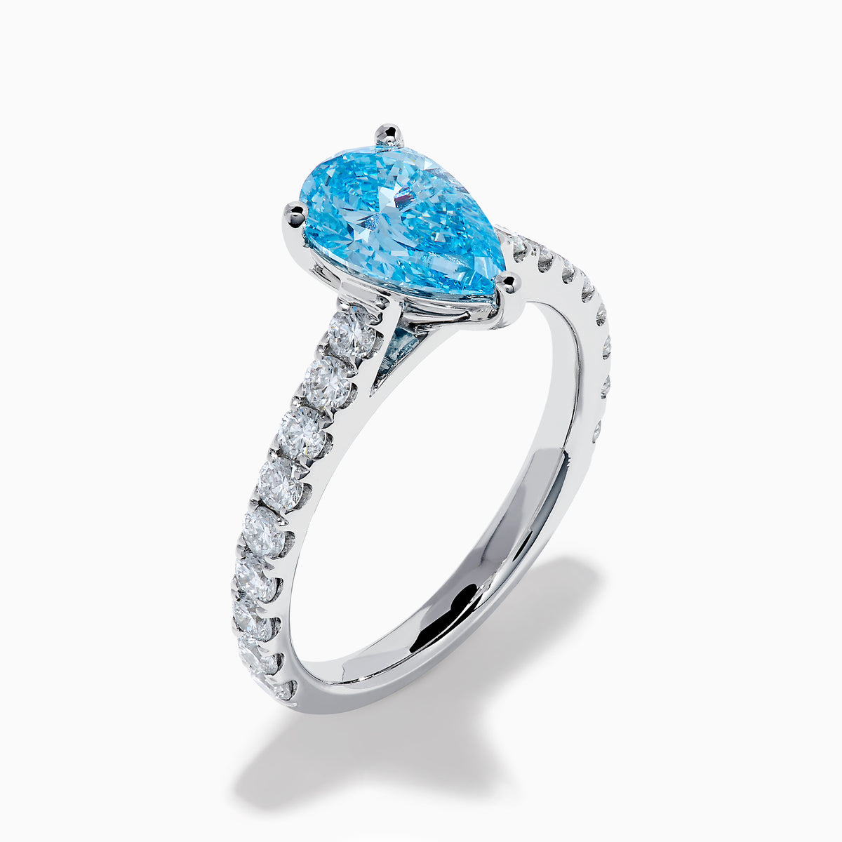 The Lab Grown Blue Diamond Solitaire Pear Ring in 14K White Gold features a striking pear-shaped blue diamond at the center, accented by a band adorned with small round white diamonds.