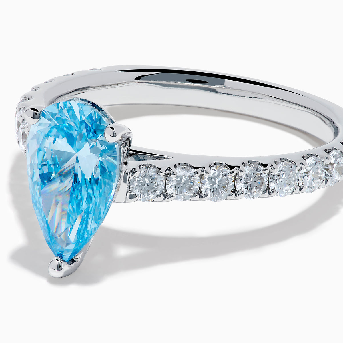The Lab Grown Blue Diamond Solitaire Pear Ring in 14K White Gold features a striking pear-shaped blue diamond at the center, accented by a band adorned with small round white diamonds.