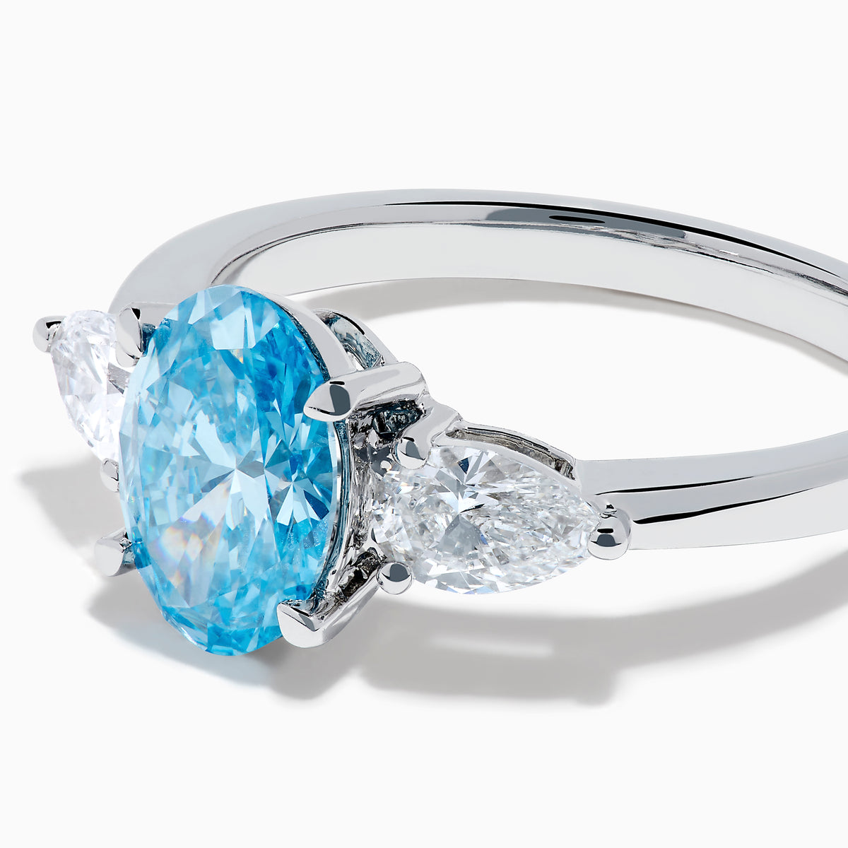 The Lab Grown Blue and White Diamond 3-Stone Ring in 14K White Gold showcases an oval blue centerpiece with two pear-shaped lab grown diamonds on each side, all set in elegant white gold.