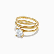 The Lab Grown Diamond Wrap around Round Ring in 14K Yellow Gold features a twisted triple-band design with a large round diamond center, shown against a white background.