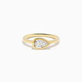 The Lab Grown Diamond East West Pear Ring in 14K Yellow Gold showcases a lab diamond in a pear shape, set horizontally in a sleek bezel on a plain band, presented against a white background.