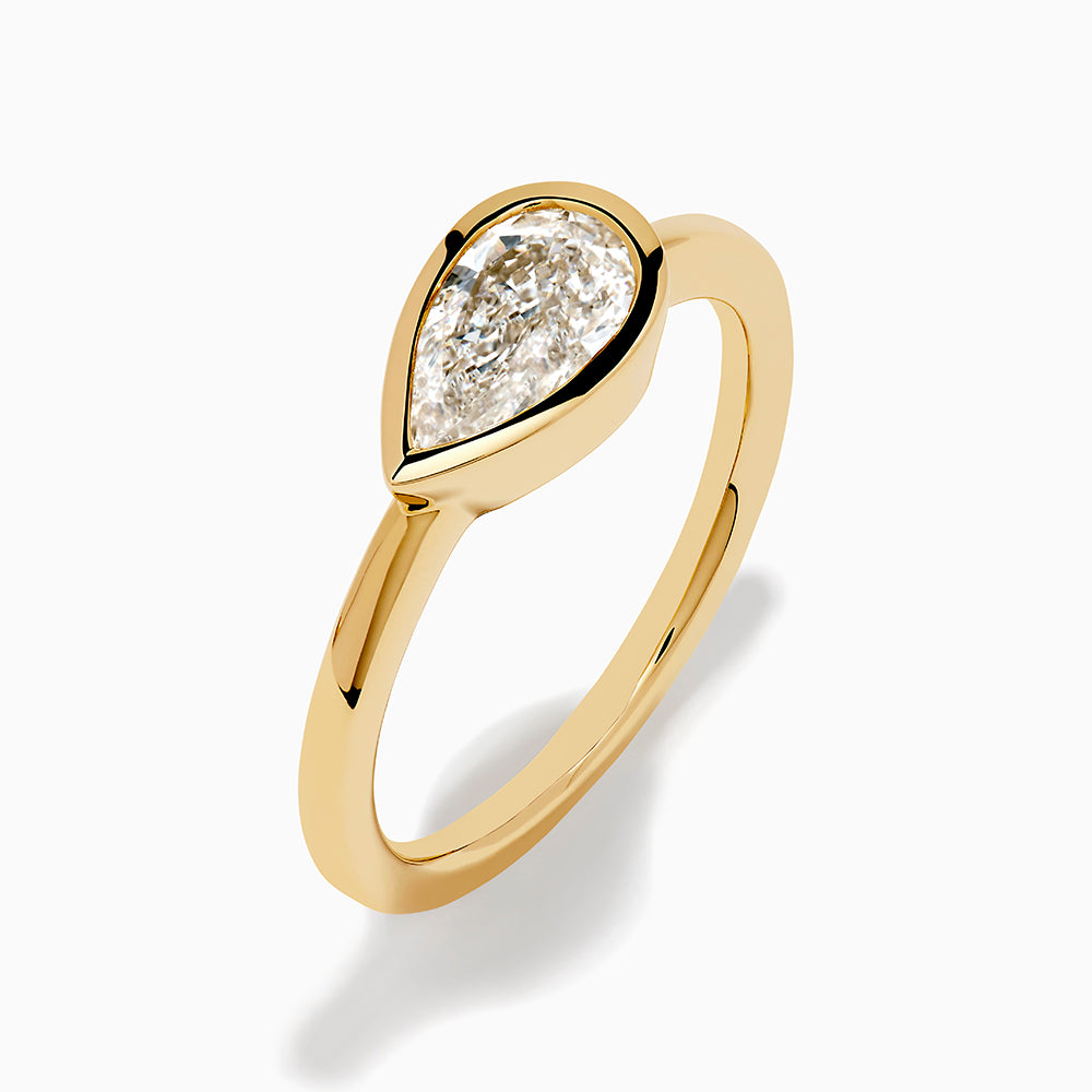 The Lab Grown Diamond East West Pear Ring in 14K Yellow Gold showcases a lab diamond in a pear shape, set horizontally in a sleek bezel on a plain band, presented against a white background.
