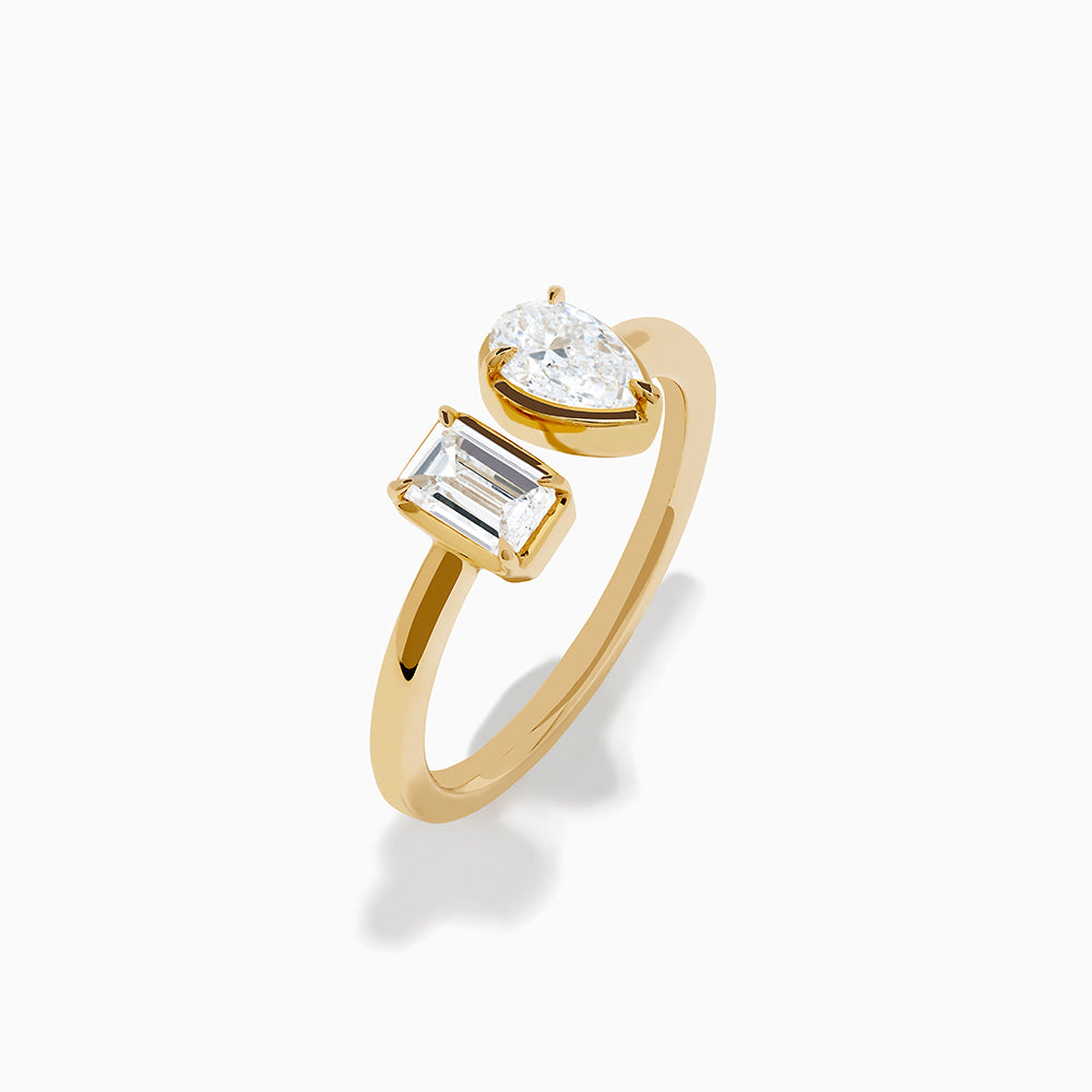 The Lab Grown Diamond Toi Et Moi Ring in 14K Yellow Gold features a pear-shaped diamond and an emerald-cut lab diamond set side by side on a plain gold band, displayed on a white background.