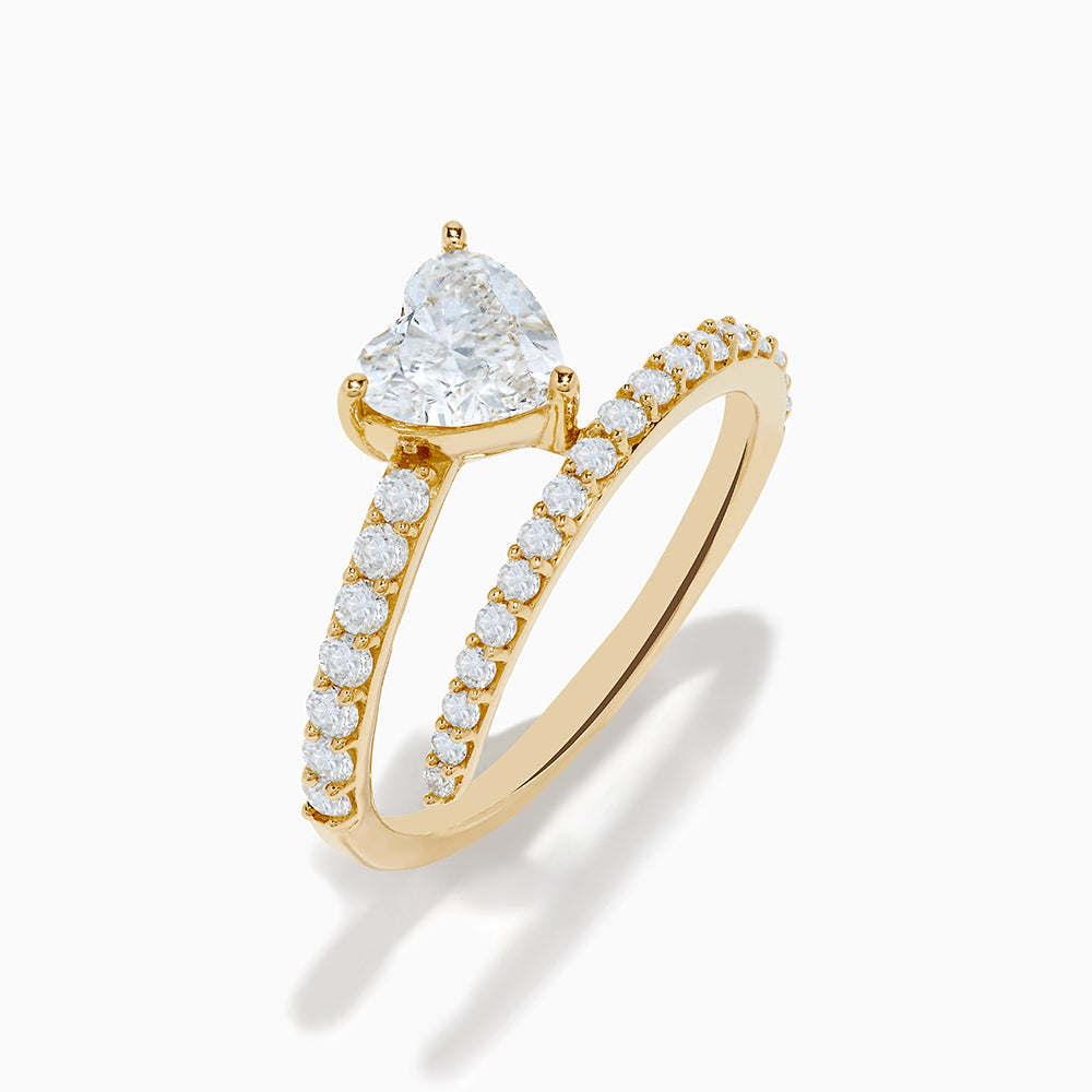 The Lab Grown Diamond Wrap Around Heart Ring in 14K Yellow Gold showcases a heart-shaped center stone and two open bands adorned with diamonds, elegantly displayed on a white background.