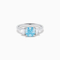 A Lab Grown Blue and White Diamond 3 Stone Ring in 14K White Gold showcases a central rectangular blue diamond flanked by two clear rectangular diamonds, set in gleaming white gold and displayed against a white background.
