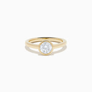 The Lab Grown Round Diamond Bezel Ring in 14K Yellow Gold features a simple band with a single bezel-set round white diamond at the center, shown on a white background.