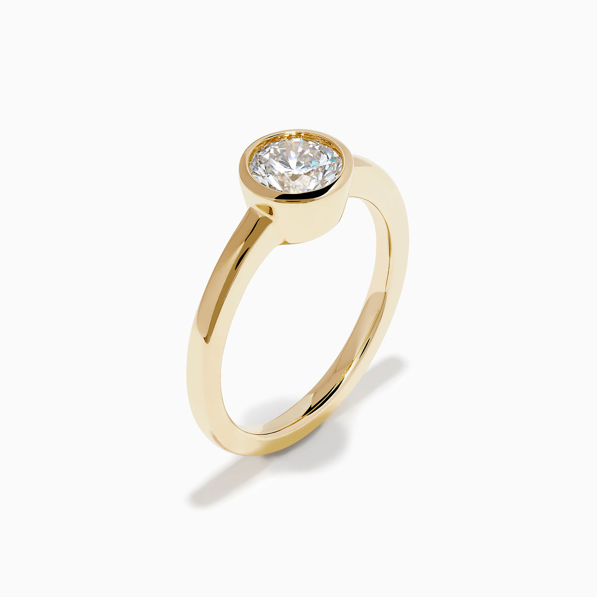 The Lab Grown Round Diamond Bezel Ring in 14K Yellow Gold features a simple band with a single bezel-set round white diamond at the center, shown on a white background.