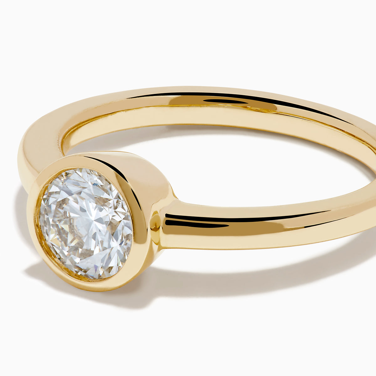 The Lab Grown Round Diamond Bezel Ring in 14K Yellow Gold features a simple band with a single bezel-set round white diamond at the center, shown on a white background.