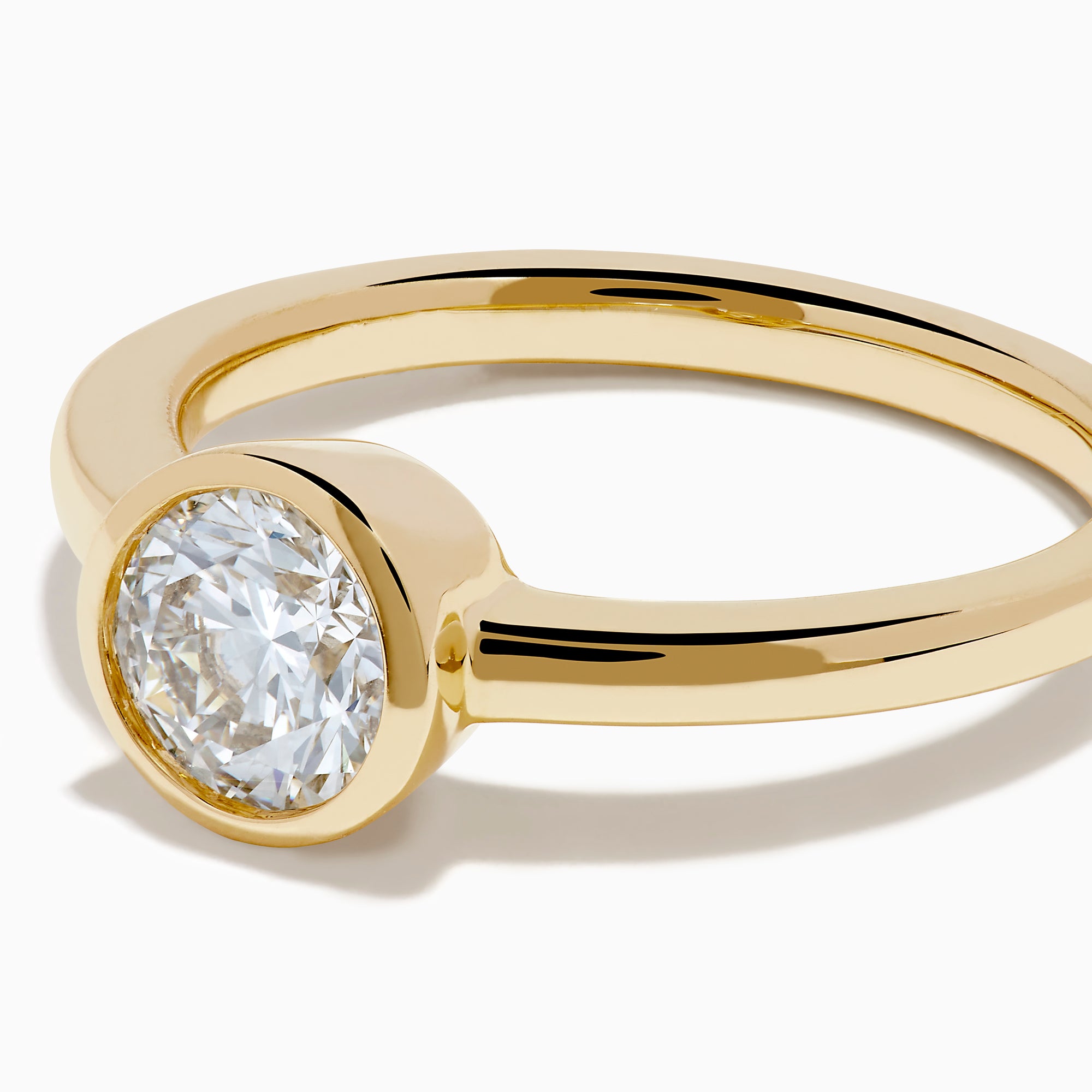 The Lab Grown Round Diamond Bezel Ring in 14K Yellow Gold features a simple band with a single bezel-set round white diamond at the center, shown on a white background.