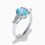 The Lab Grown Blue and White Diamond 3-Stone Ring in 14K White Gold showcases an oval blue diamond flanked by tapered white baguette diamonds, all set against a plain white background.