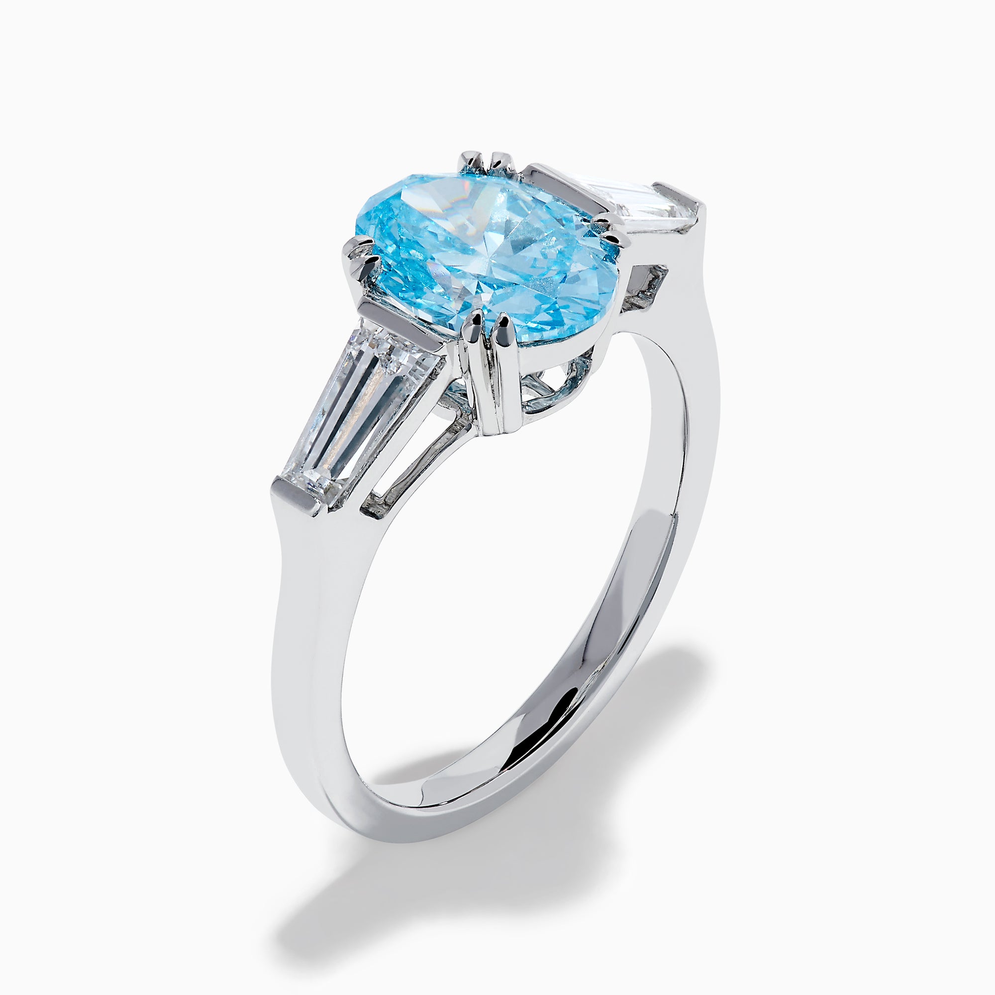 The Lab Grown Blue and White Diamond 3-Stone Ring in 14K White Gold showcases an oval blue diamond flanked by tapered white baguette diamonds, all set against a plain white background.